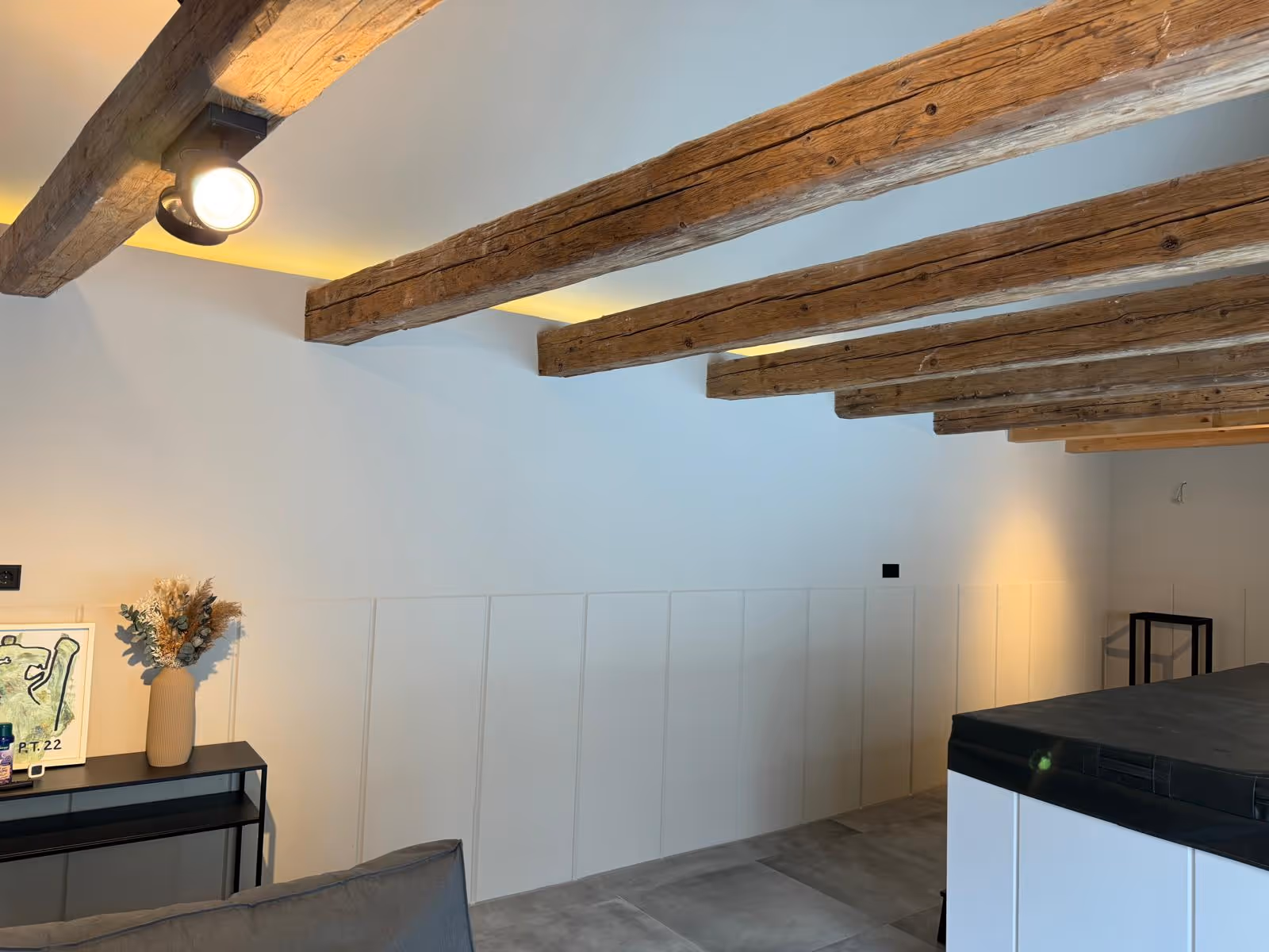 Aufgearbeitete Holzbalken mit Strahlern über weißer Wandverkleidung in der sanierten Scheune
