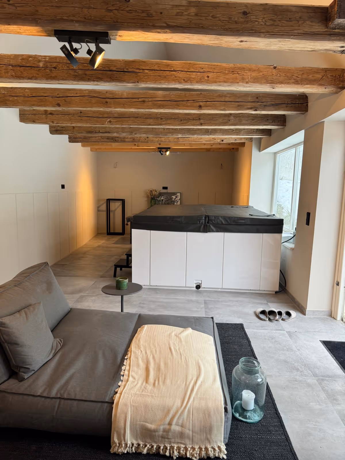 Langgestreckter Raum mit freigelegten Deckenbalken, Loungesofa und Whirlpool in der Augsburger Scheune