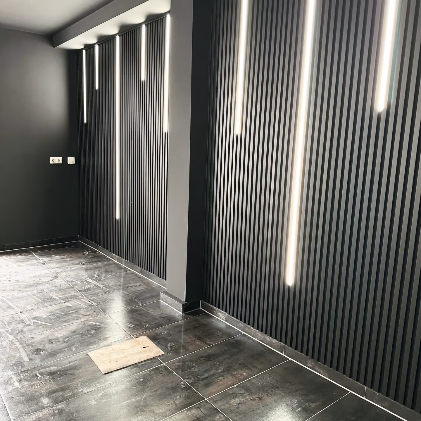 Dunkle Lamellenwände mit senkrechten LED-Leisten über dunklem Fliesenboden