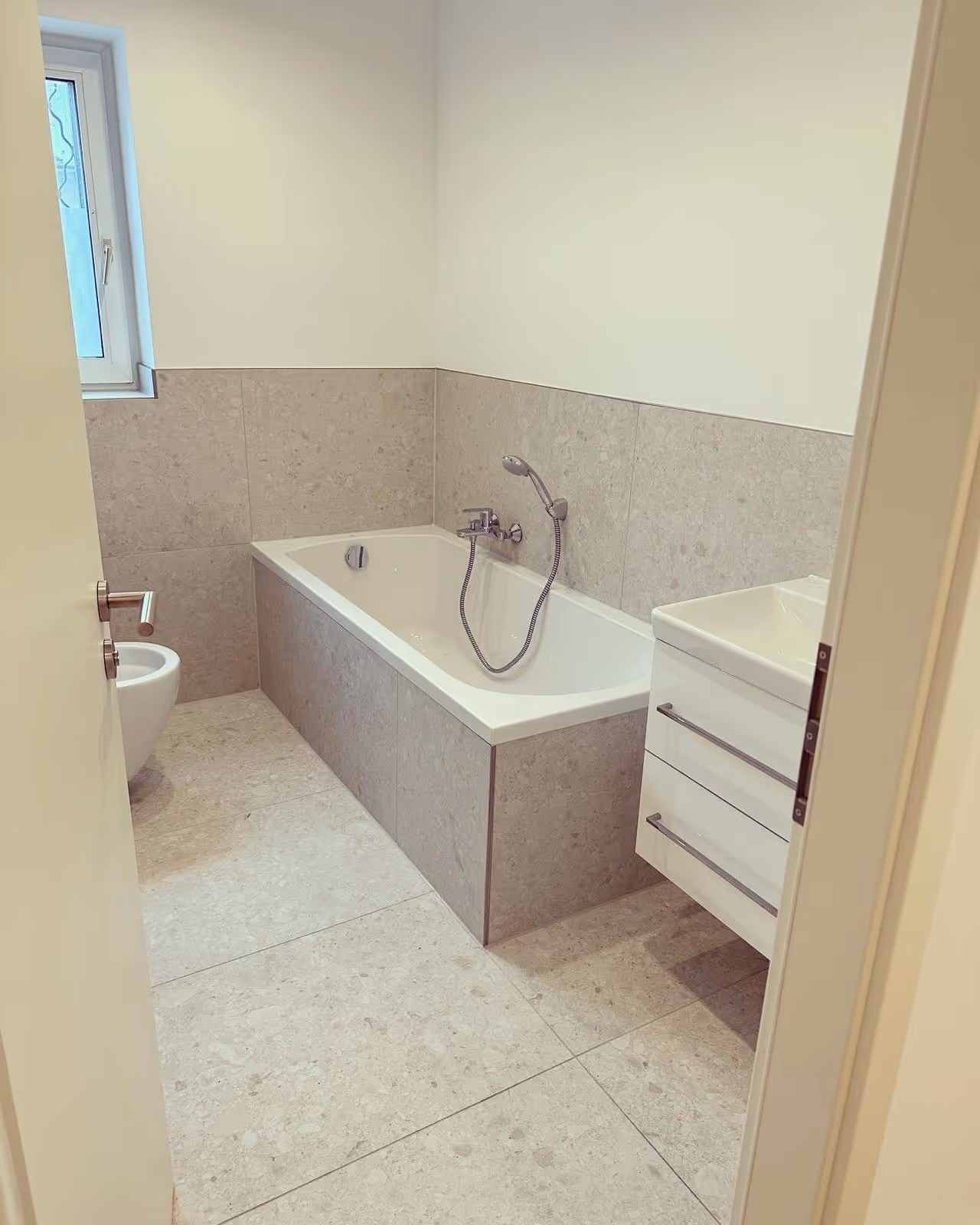 Badezimmer mit eingebauter Badewanne und Fliesen in Terrazzo-Optik, Kernsanierung München