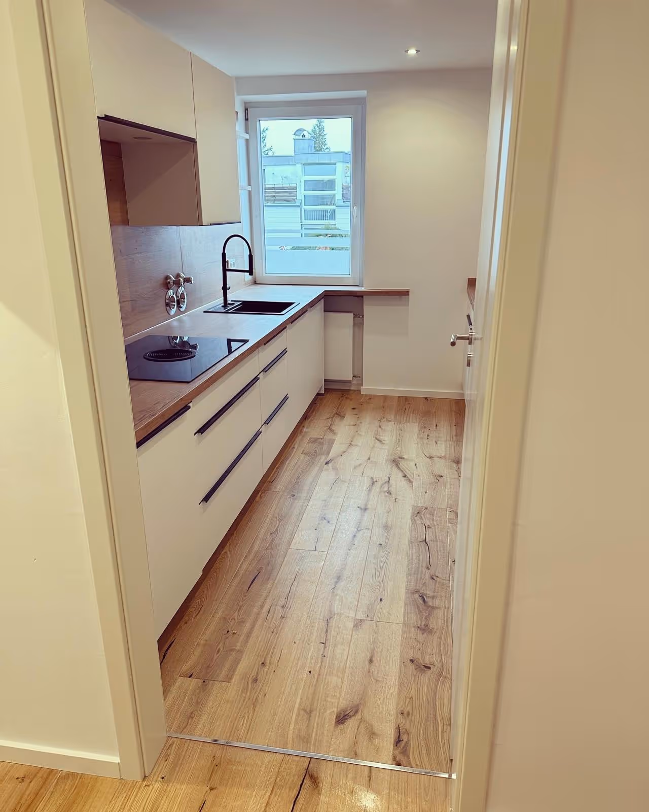 Schmale Küche mit weißen Fronten und Holzdielen nach der Kernsanierung in München