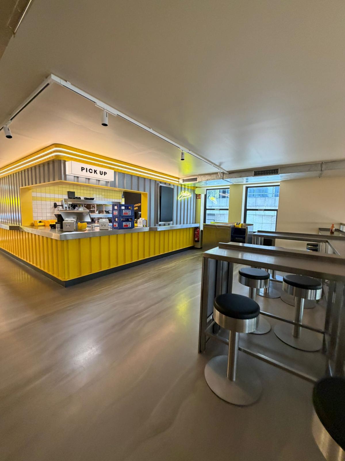 Gastraum mit gelbem Tresen, Stehtischen und Lichtschienen im Goldies Smashburger in München