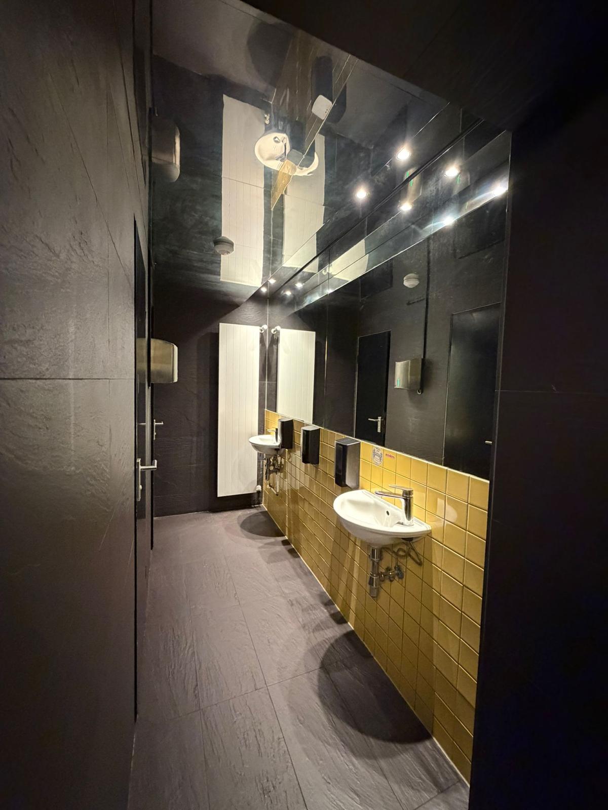 Gäste-WC mit dunklen Wänden und beleuchtetem Spiegel nach dem Umbau des Restaurants in München