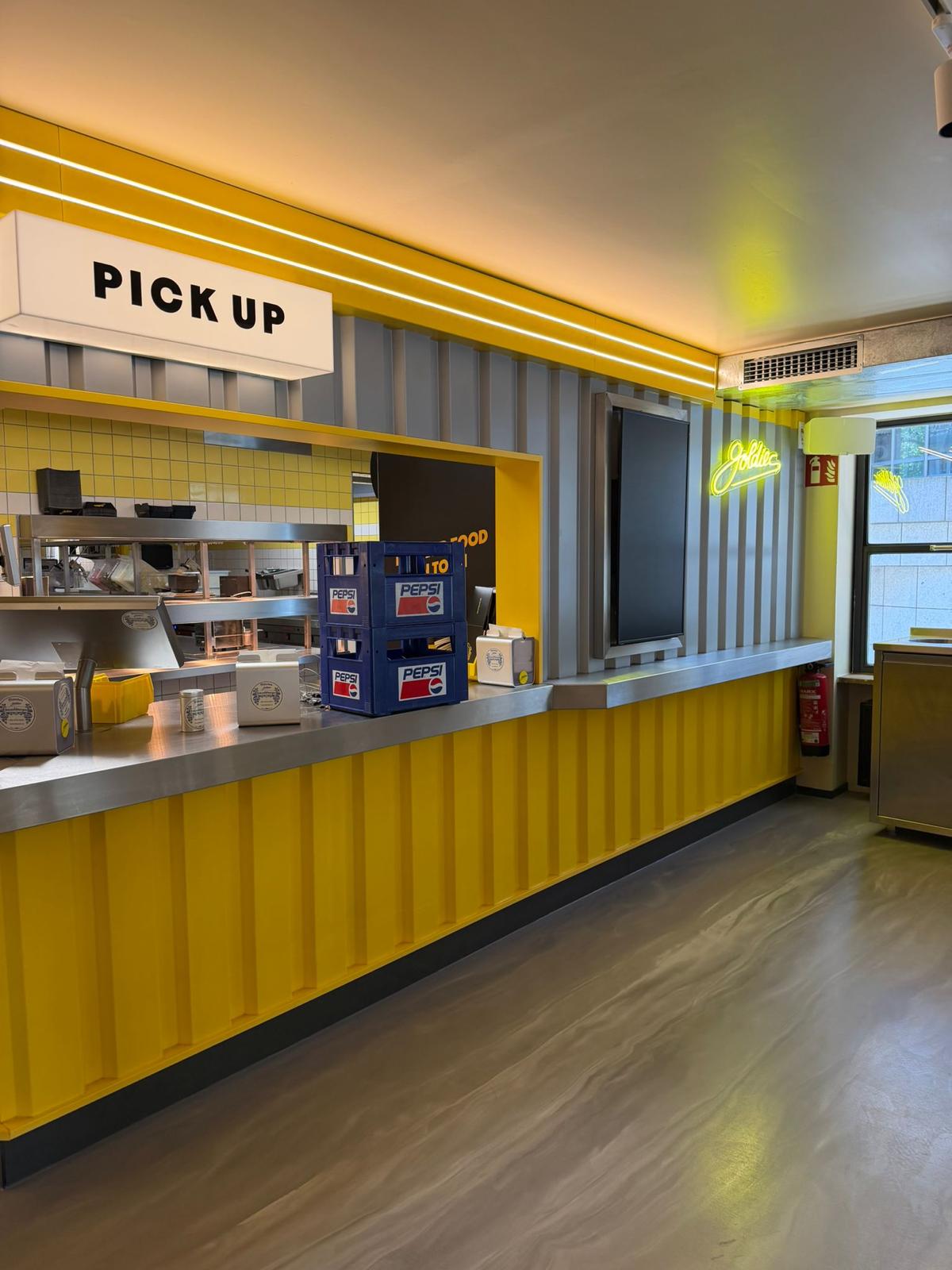 Ausgabetresen mit Pick-up-Schild und gelber Verkleidung im umgebauten Restaurant in München