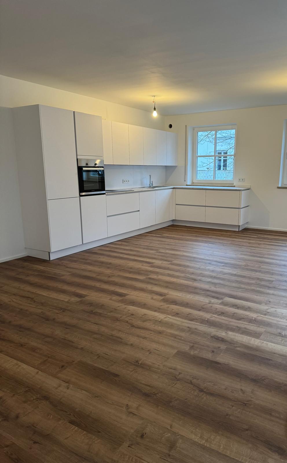 Wohnbereich mit weißer Küchenzeile und Holzboden in einer modernisierten Eigentumswohnung in Augsburg