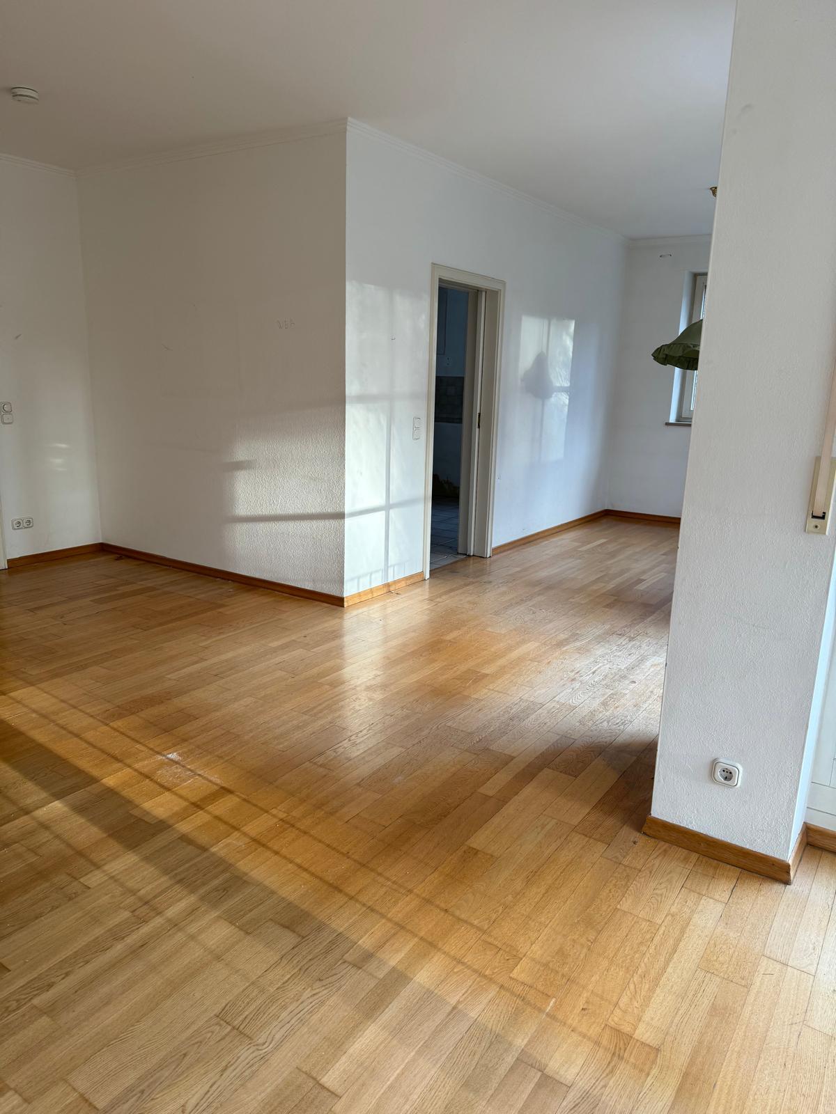 Wohnraum mit aufgearbeitetem Parkett und weißen Wänden nach der Modernisierung in Augsburg