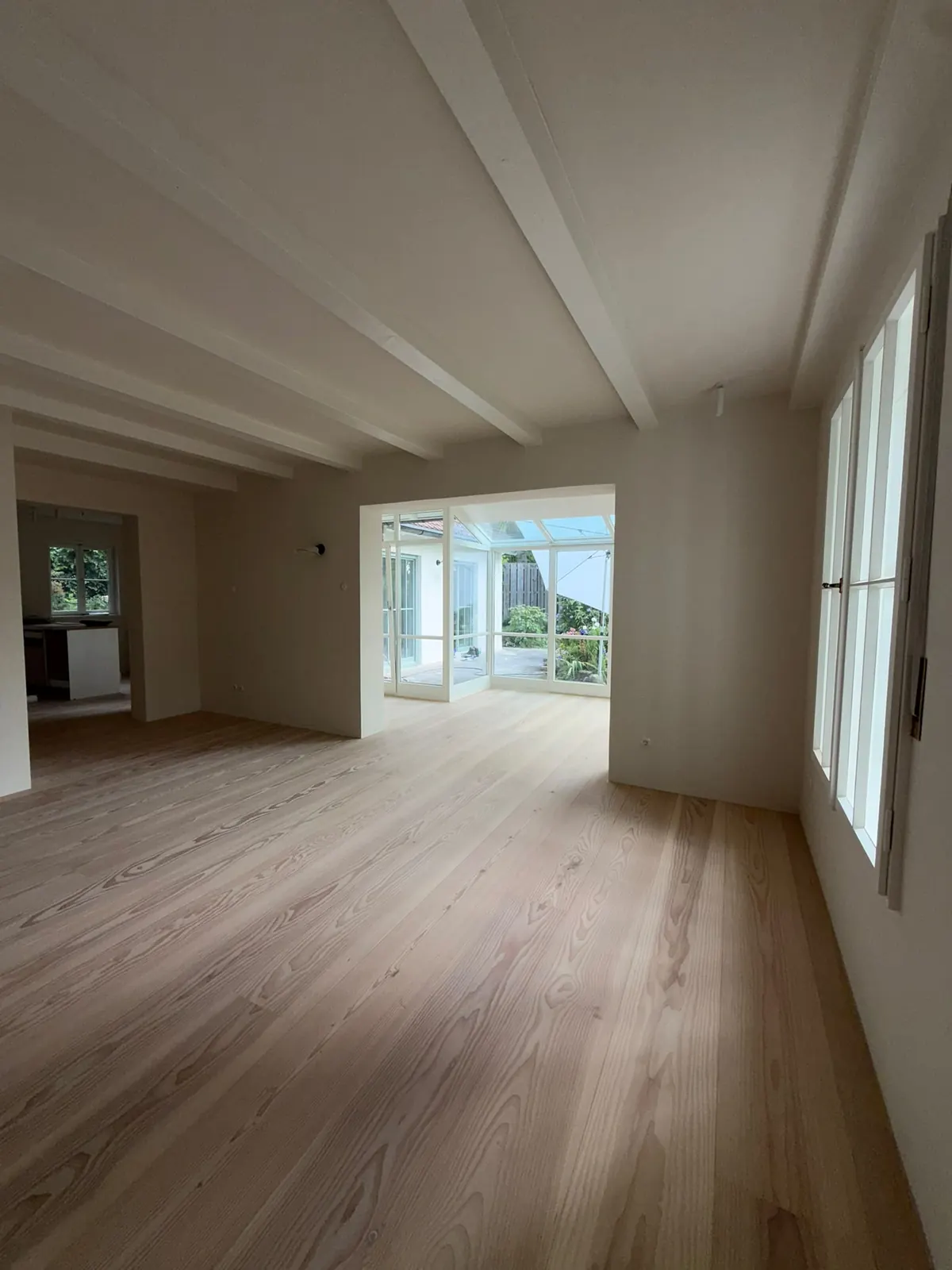 Haus am Pilsensee nach der Sanierung: heller Wohnbereich mit Holzboden und Durchgang zum Wintergarten