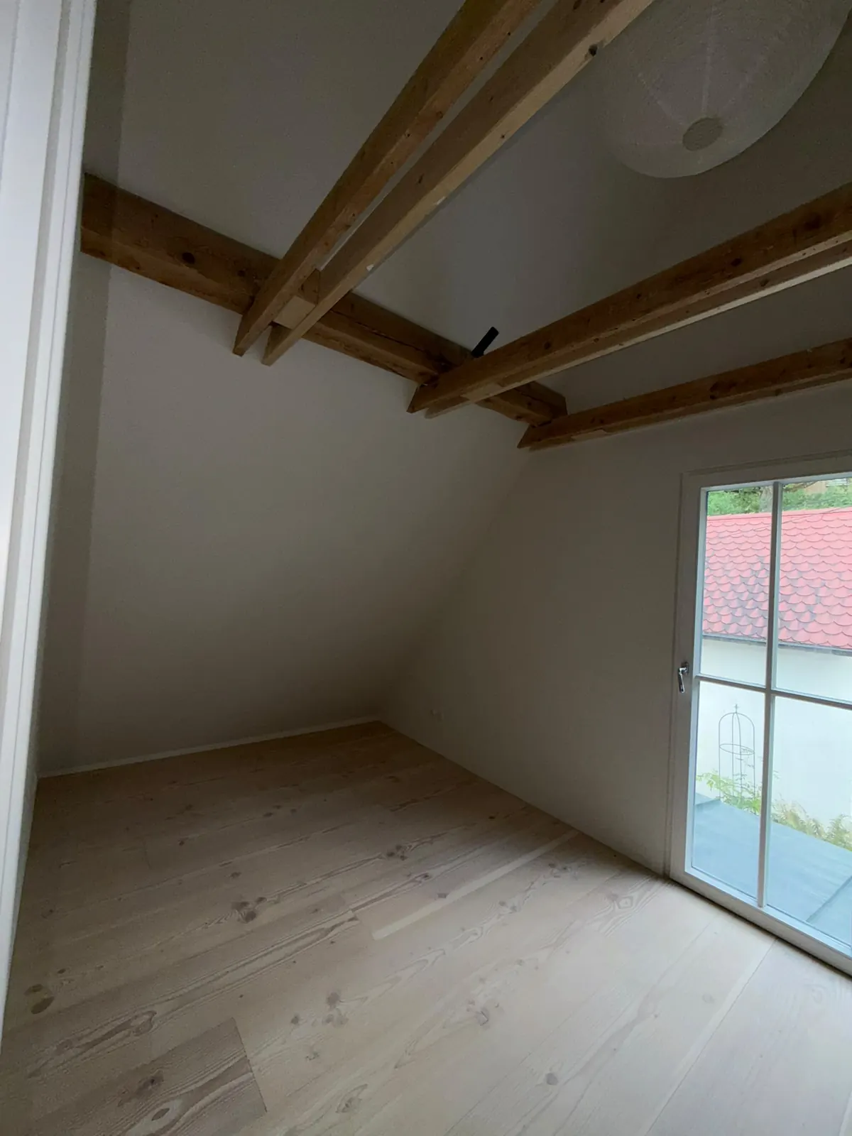 Schlafzimmer im Dachgeschoss am Pilsensee nach der Sanierung mit sichtbaren Holzbalken, Holzdielen und Fenstertür