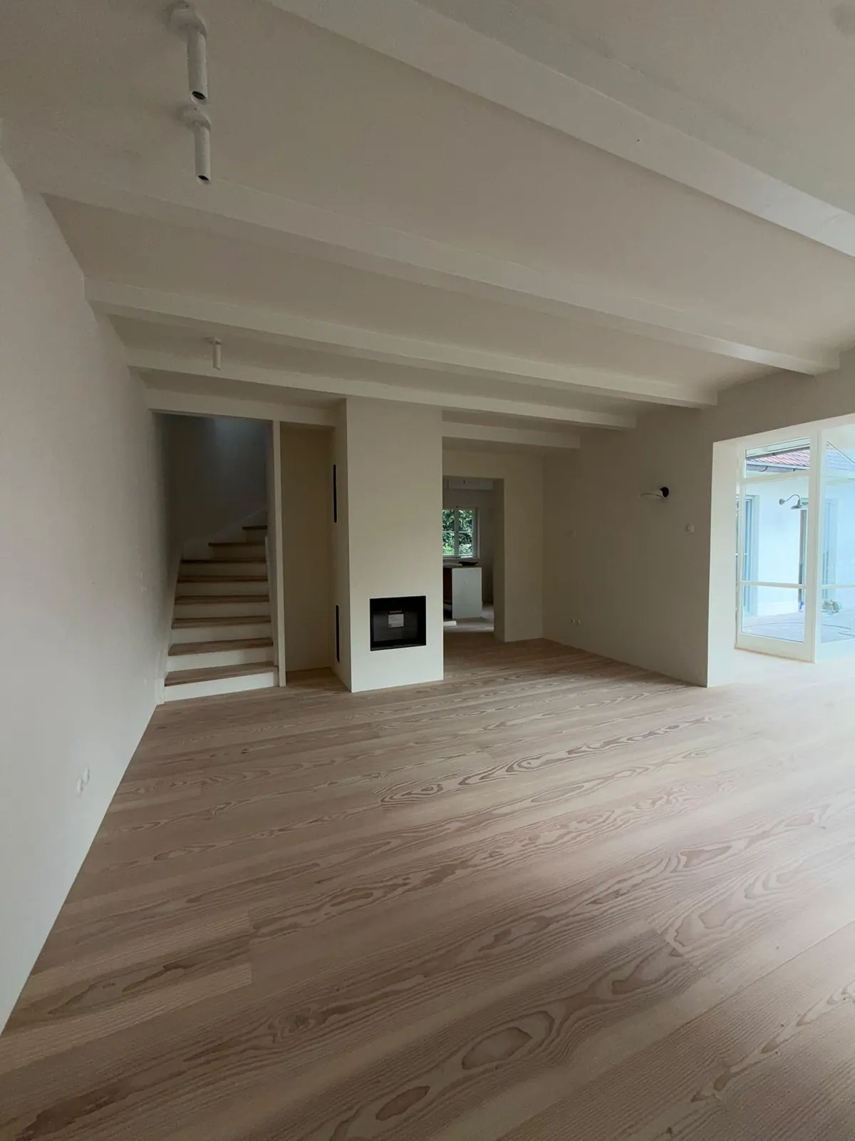Offener Wohnbereich mit Kamin, Treppe und Holzboden nach der Sanierung am Pilsensee